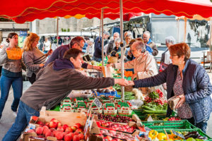 Echange de monnaie entre une commerçante et une cliente sur un marché de plein air.